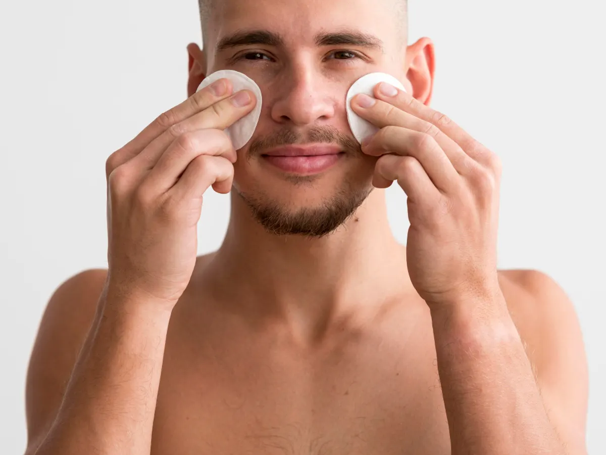 Homme appliquant un soin sur son visage avec des cotons